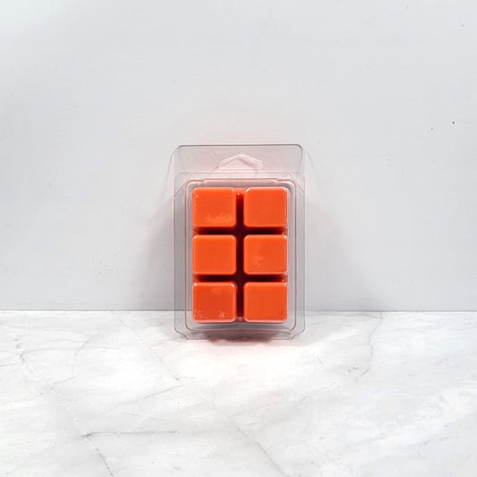 Pack of orange wax melts in a clear plastic packaging on a white marble surface.